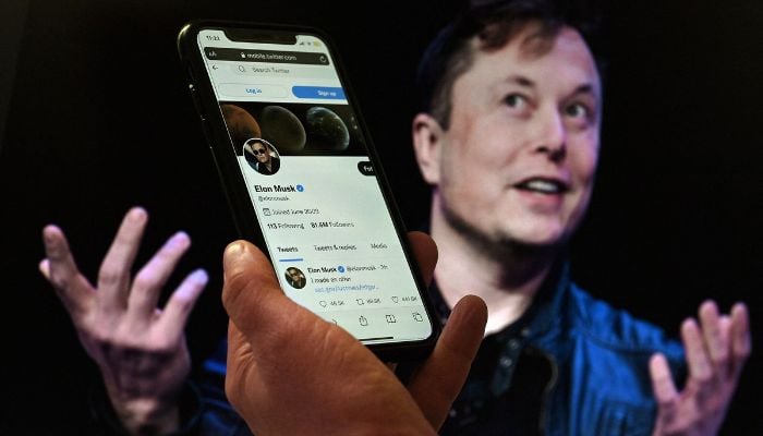 A phone screen displays the Twitter account of Elon Musk in front of a photo of him in the background in this illustration, Washington, DC, US, April 14, 2022. — AFP