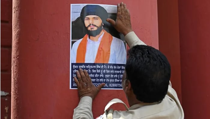 Bu tarihsiz dosya fotoğrafında bir polis yetkilisi, Amritsar'daki bir tren istasyonuna Khalistan yanlısı lider Amritpal Singh için aranan bir poster asıyor.  — AFP