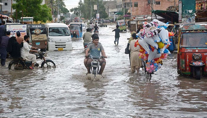 9 Temmuz 2022'de Karaçi'nin Korangi bölgesinde bir yolda biriken yağmur sularından geçen motosikletliler. Fotoğraf: APP