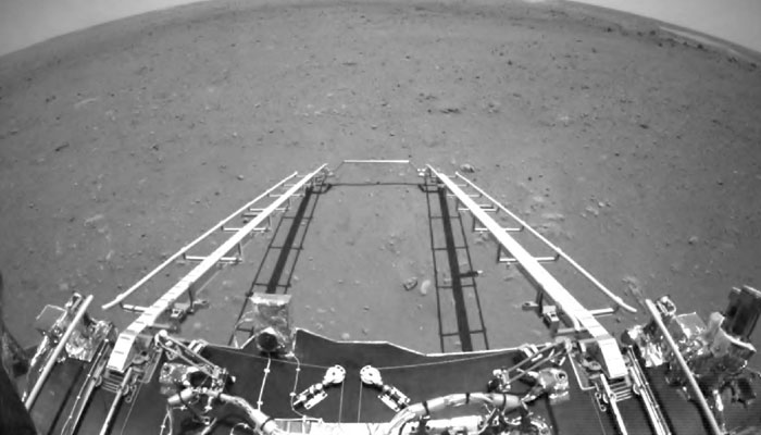 Çin Ulusal Uzay İdaresi (CNSA) tarafından 19 Mayıs 2021'de yayınlanan bu resim, Çin'in Zhurong gezgininin ön engellerden kaçınma kamerası tarafından çekilen, gezginin hareket yönüne bakan ve rampa mekanizmasının konuşlandırılmasını gösteren bir görüntüyü gösteriyor. 15 Mayıs 2021'de Mars'a indikten sonra Mars yüzeyi. - AFP