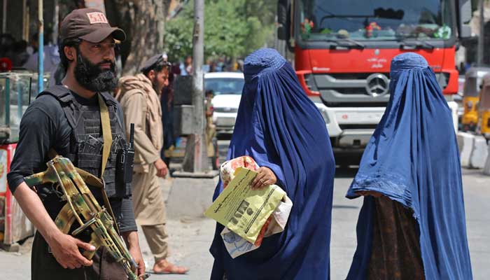 30 اپریل 2023 کو جلال آباد کی ایک سڑک پر برقعہ پہنے ایک افغان خاتون طالبان کے سیکیورٹی گارڈ کے پاس سے گزر رہی ہے۔ - اے ایف پی