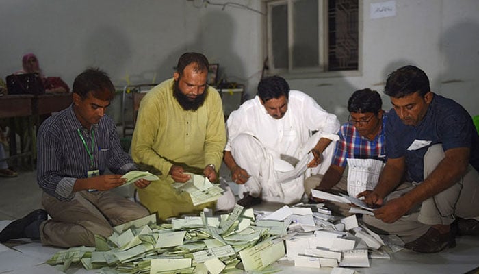Seçim yetkilileri, 25 Temmuz 2018'de Karaçi'deki bir sandık merkezinde sandıklar kapandıktan sonra oy pusulalarını sayıyor. — AFP