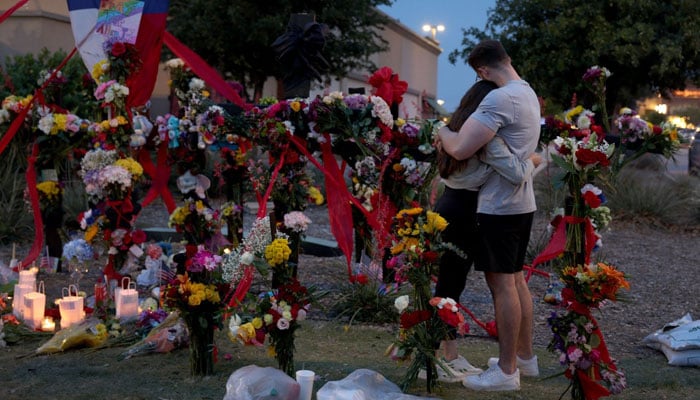 ایلن، ٹیکساس، USA، 7 مئی 2023 میں فائرنگ کے متاثرین کی یادگار پر جاتے ہوئے لوگ گلے لگا رہے ہیں۔ AFP