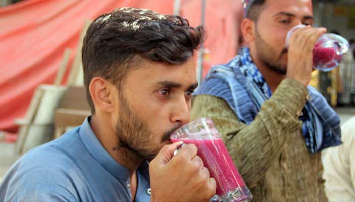 People drink phalsa juice beside a street vendors kiosk in Karachis Orangi Town area to cool down during hot weather in the city on May 5, 2023. — Online