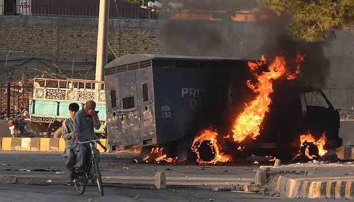 Men on a bike ride past a burning police vehicle during a protest by Pakistan Tehreek-e-Insaf party activists and supporters of former Pakistan´s Prime Minister Imran against the arrest of their leader, in Quetta on May 9, 2023. — AFP