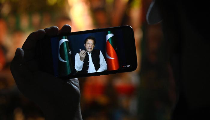 PTI partisinin bir aktivisti, 13 Mayıs 2023'te Lahor'daki Zaman Park'ta eski başbakan Imran Khan'ın konuşmasını telefonda dinliyor. — AFP