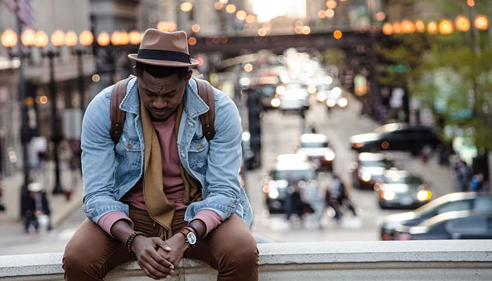 A man sits worried on a bridge, overlooking a busy street. — Unsplash/File