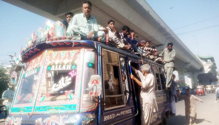 30 Kasım 2022'de Karaçi'de aşırı yüklü bir otobüsün çatısında seyahat eden yolcular. — PPI