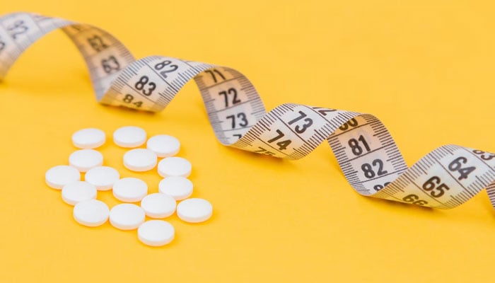 Gambar ini menunjukkan pil obat yang ditampilkan di sebelah pita pengukur.  — Hapus percikan/File