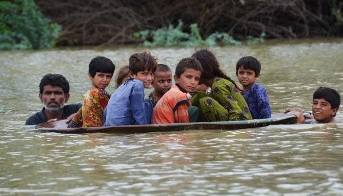 A man (left) along with a youth use a satellite dish to move children across a flooded area after heavy monsoon rainfalls in Jaffarabad, Balochistan, on August 26, 2022. — AFP