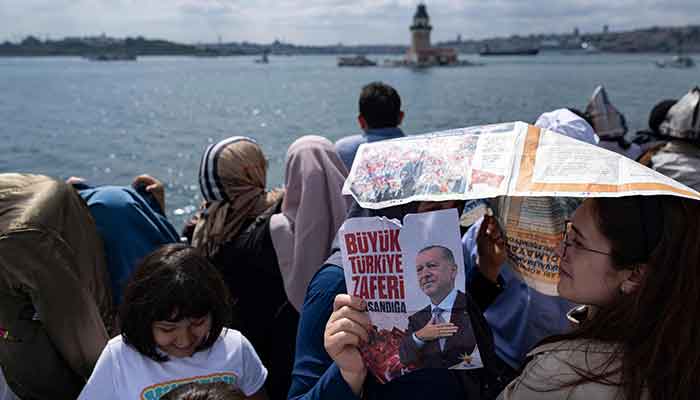 A woman holding a poster depicting Turkish President Recep Tayyip Erdogan waits in the queue at the Maidens Tower, which was reopened to visitors after the restoration, ahead of the May 28 presidential runoff vote, in Istanbul on May 27, 2023. — AFP
