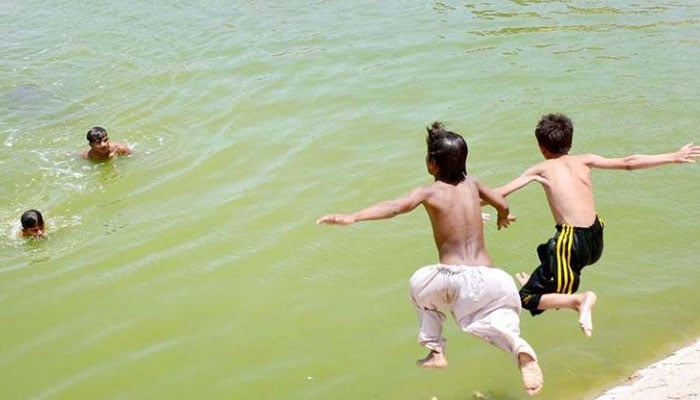 Youngsters jumping into a water pond in Hyderabad. — APP/File