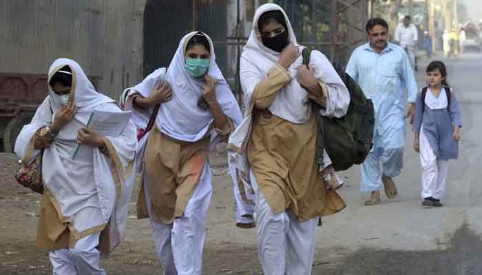 Students wearing facemasks walk through a street to their school in Peshawar on September 15, 2020. — AFP