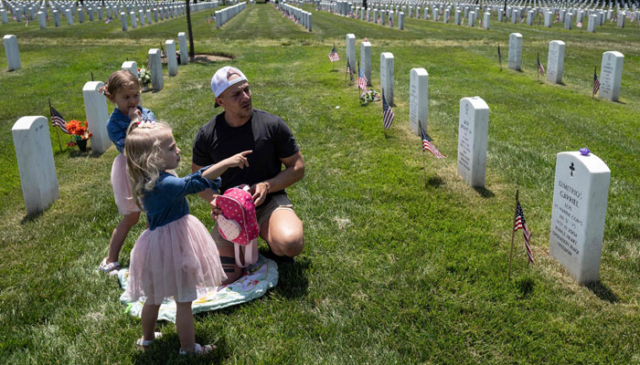 A man visits friends he lost in the 2004 Battle of Fallujah, with his daughters in Section 60 of Arlington National Cemetery, prior to Memorial Day weekend, in Arlington, Virginia, May 26, 2023. — AFP