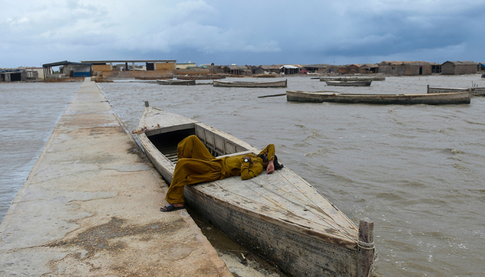 A man rests on a boat moored along the Arabian Seas coast, at the Zero Point in Badin district, Sindh province on June 15, 2023. — AFP