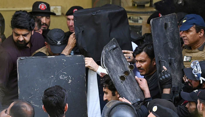 Security personnel use bulletproof shields to protect the former prime minister as he arrives at the high court in Islamabad on March 27, 2023. — AFP