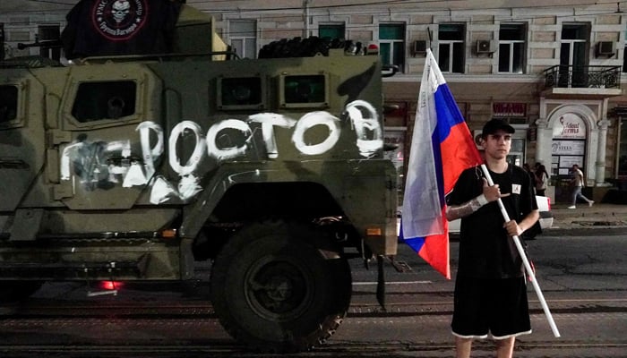 A man holds the Russian national flag in front of a Wagner group military vehicle with the sign read as Rostov in Rostov-on-Don late on June 24, 2023. — AFP