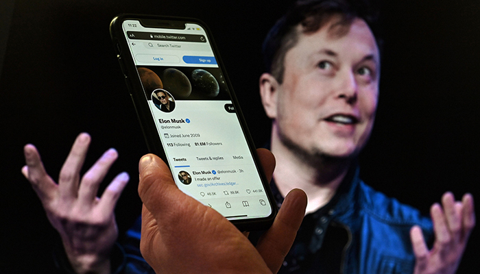In this photo illustration, a phone screen displays the Twitter account of Elon Musk with a photo of him shown in the background on April 14, 2022 in Washington, DC. — AFP