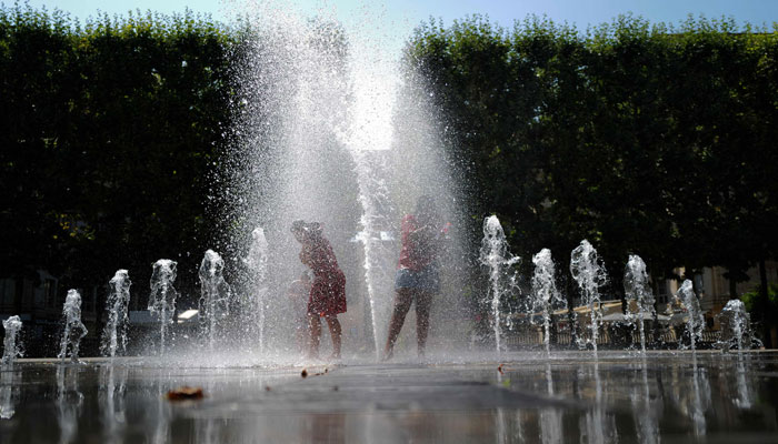 Children cool off under water jets in a fountain during a heatwave in Montpellier, southern France, on June 26, 2023. — AFP