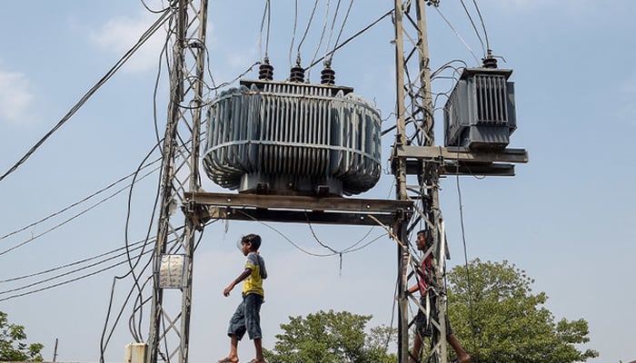 Two boys walk on a wall near high voltage electricity wires in Rawalpindi, Pakistan, on July 8, 2020. — AFP