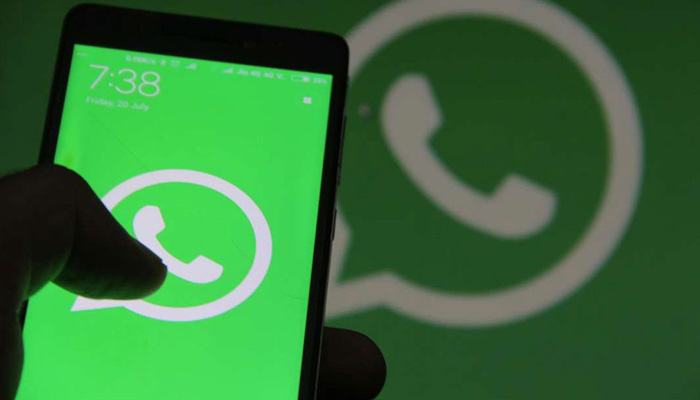 A hand holding a smartphone with the WhatsApp logo on its screen and in the background in this undated photo. — AFP/File