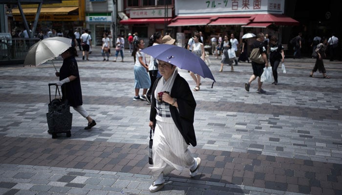 An elderly woman holds an umbrella to shield herself from sunlight as she walks along a street in Tokyo. AFP/File