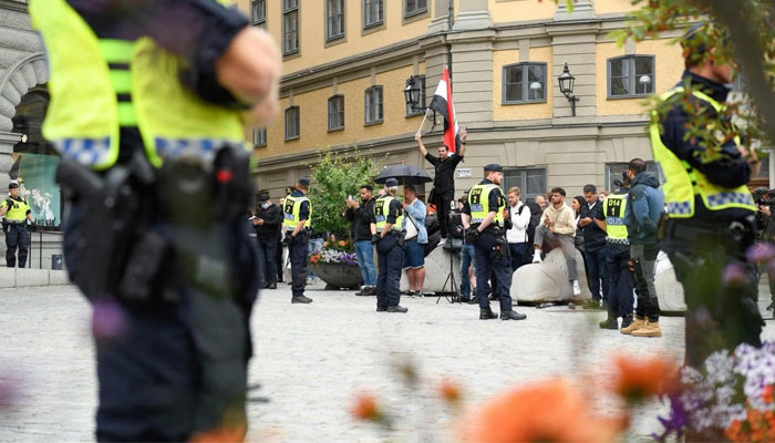 Policemen stand next to demonstrators, among them a protester (background, C) holding the flag of Iraq, at Mynttorget square in Stockholm, Sweden, on July 31, 2023. — AFP