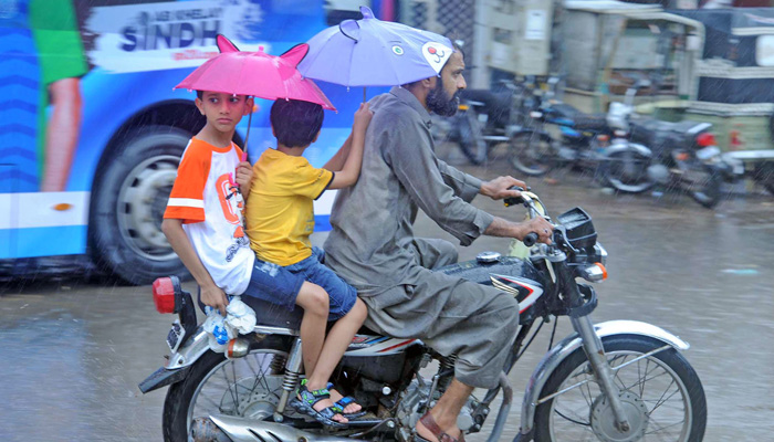Man rides a motorbike with his kids at the back during heavy rainfall in Hyderabad on July 24, 2023. — Online