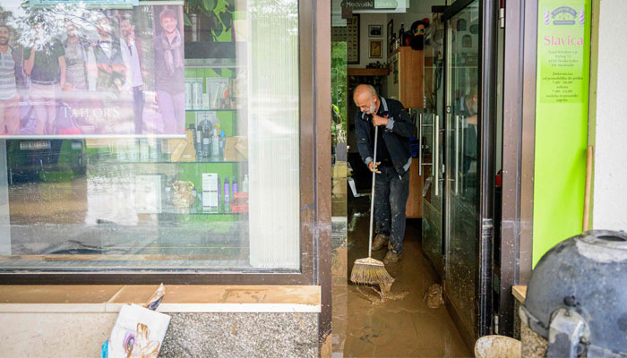 A man cleans mud off at a shop following a flood caused by heavy rains in the town of Medvode, central Slovenia, on August 4, 2023. — AFP