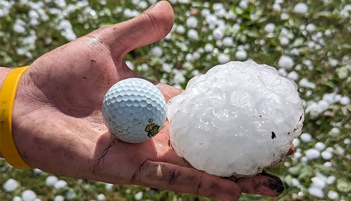 The baseball-sized hailstone next to a golf ball. — Facebook/@Derek Hasselberg