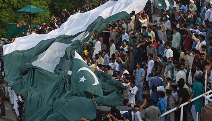 People carry a giant Pakistani flag while watching ´Beating the Retreat´ ceremony on the eve of the country´s Independence Day celebrations at the Pakistan-India Wagah border post, about 35km from Lahore on August 13, 2023. — AFP