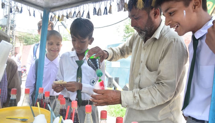 Students buy gola ganda from a street vendor outside their school in Rawalpindi on August 22, 2023. — Online
