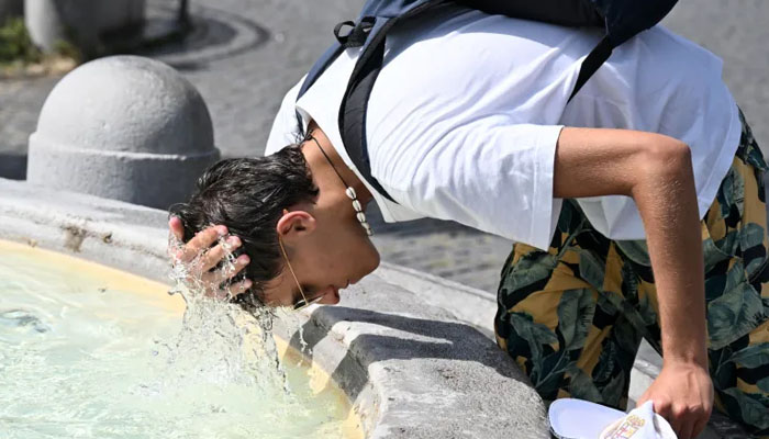 A boy pours water over his head to cool off at a fountain in Italy. — AFP