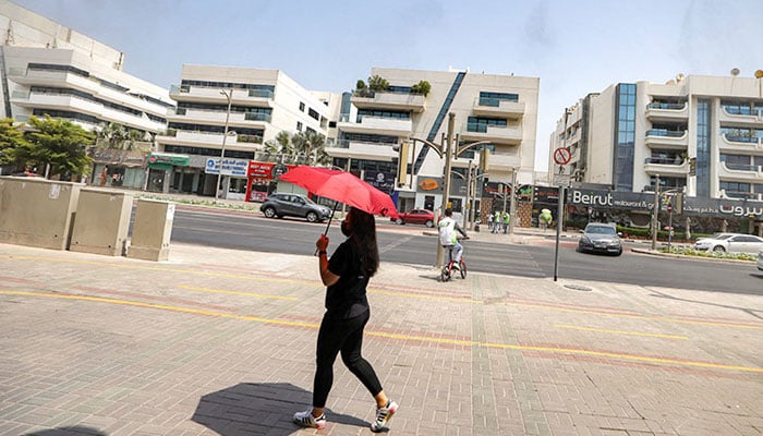 A woman walks with an umbrella underneath sprinklers releasing water vapour along a street to relieve pedestrians in Dubai. —AFP/file