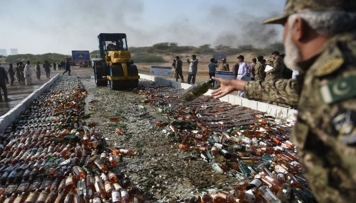 A Pakistani official uses a steamroller to crush bottles of liquor in the outskirts of Karachi on February 20, 2020. — AFP
