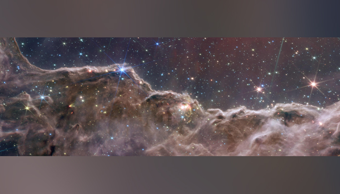 یہ تصویر 12 جولائی، 2022 کو جاری کی گئی، اور جیمز ویب اسپیس ٹیلی سکوپ (JWST) کے ذریعے لی گئی ایک پہاڑی اور وادی کا علاقہ دکھاتا ہے جو روشن ستاروں سے بندھی ہوئی ہے جو کہ NGC کہلانے والے قریبی، نئے، ستارے بنانے والے خطے کا کنارہ ہے۔  کیرینا نیبولا میں 3324۔  - اے ایف پی