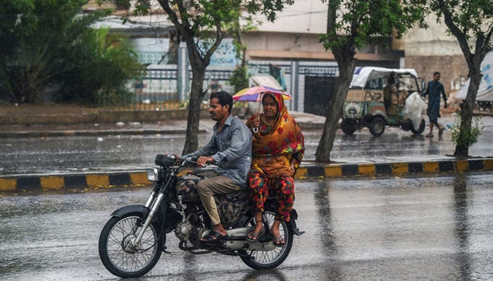 Commuters make their way amid rain showers in Karachi, Pakistan, on June 15, 2023. — AFP