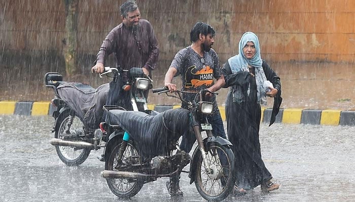 Commuters push their motorbikes along a street during a monsoon rainfall in Karachi on July 5, 2022. — AFP/File