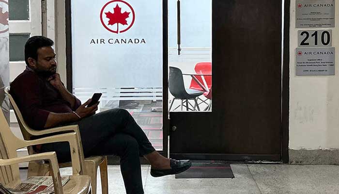 A man checks his mobile as he sits outside an Air Canada regional office in New Delhi on September 20, 2023. — AFP