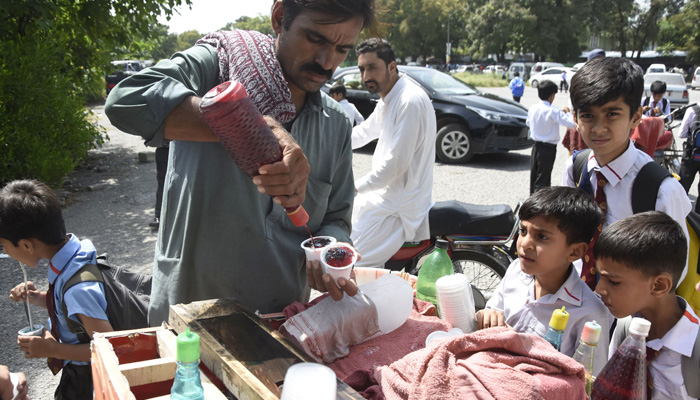 Students enjoy gola ganda after their school time from a vendor during a hot day in Islamabad on August 29, 2023. — Online