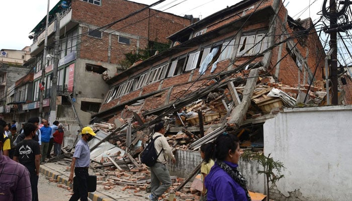 Nepalese people walk past a collapsed building in Kathmandu after an earthquake on April 25, 2015. — AFP