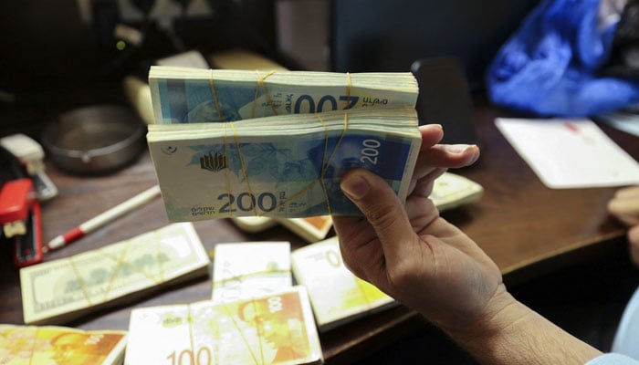 A currency dealer holds packets of Israeli currency. — AFP/File
