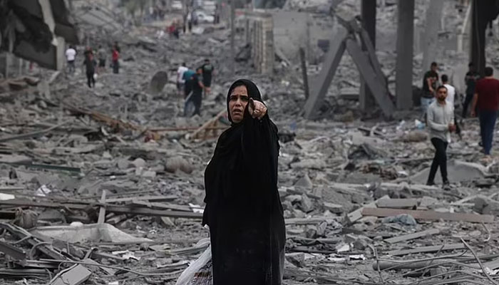 منگل کو غزہ کے شہر الرمل کے پڑوس میں اسرائیلی فضائی حملوں سے ہونے والی تباہی کے درمیان فلسطینی ملبے سے گزر رہے ہیں۔  - اے ایف پی