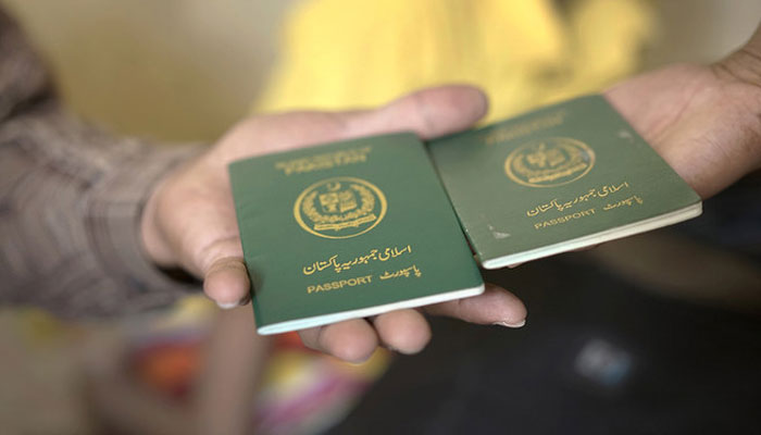 دو لوگوں کے ہاتھوں میں نظر آنے والے پاکستانی پاسپورٹ کی ایک نمائندہ تصویر۔  - اے ایف پی