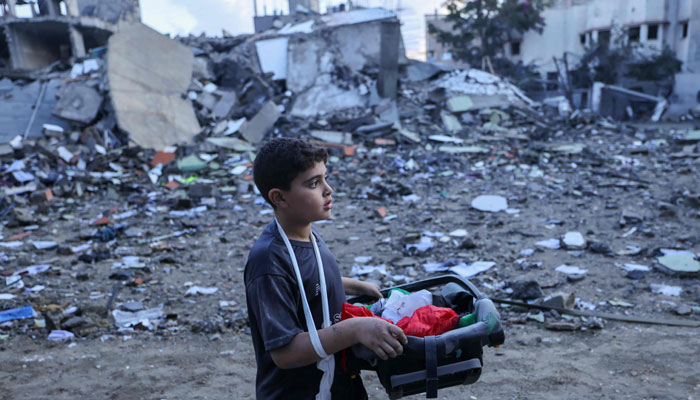 16 اکتوبر 2023 کو جنوبی غزہ کی پٹی میں رفح پناہ گزین کیمپ پر اسرائیلی حملے کے دوران تباہ ہونے والی عمارتوں کے ملبے کے درمیان ایک فلسطینی لڑکا بچاؤ کے قابل سامان رکھے ہوئے ہے۔ - اے ایف پی
