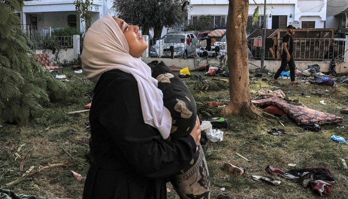 A woman reacts while holding a pillow as she stands amidst debris outside the site of the Ahli Arab Hospital in central Gaza on October 18, 2023. — AFP