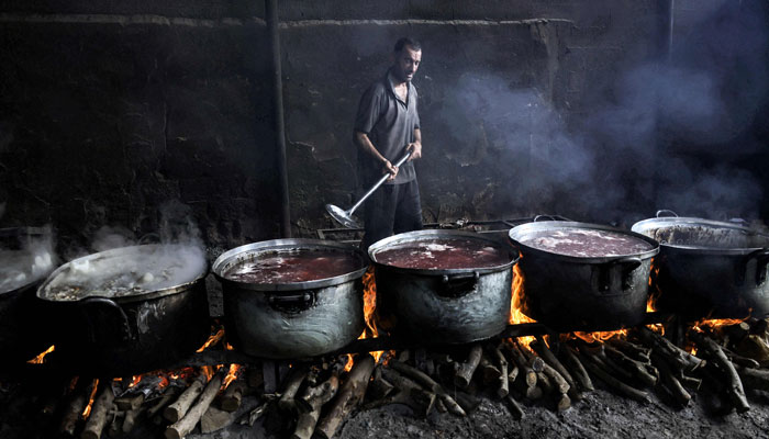 A Palestinian man stirs one of several large cooking pots simmering on wooden fires due to the lack of cooking gas, for displaced families, in Rafah, in the southern Gaza Strip on October 28, 2023, amid the ongoing battles between Israel and Palestine. — AFP