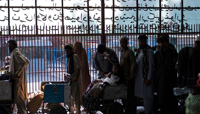 In this photo taken on October 30, 2023, Afghan people stand in a queue behind a fenced corridor at the Afghanistan-Pakistan Torkham border in Nangarhar province. — AFP