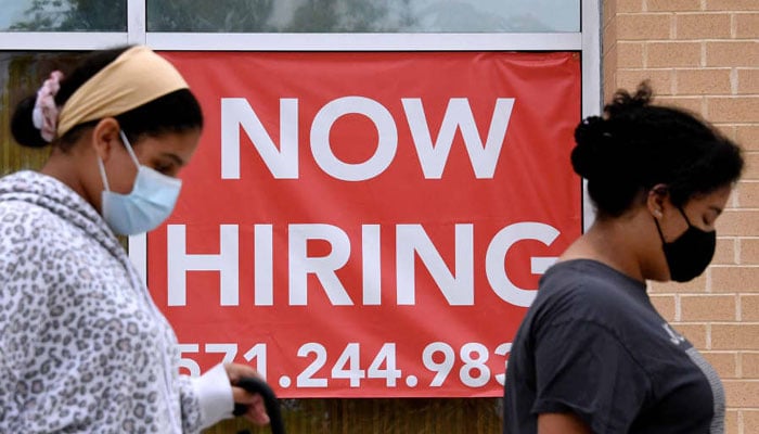 Women walk past a “Now Hiring” sign outside a store on August 16, 2021 in Arlington, Virginia. — AFP