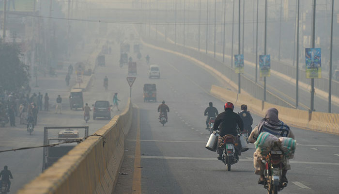Commuters make their way amid heavy smog along a road in Multan on February 16, 2023. — AFP